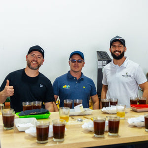 Maurizio, from Immigrant Culture and Sergio and friend from Finca Anaya standing behind a table with multiple glasses of coffee, in a coffee cupping setting